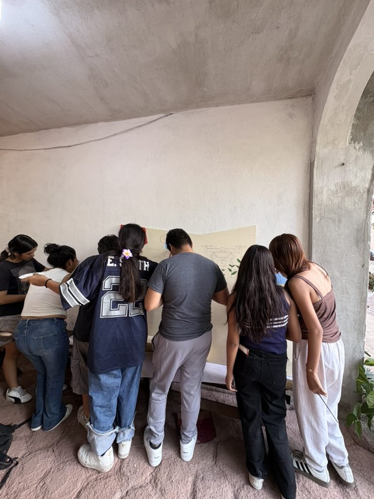 Seis personas de espaldas, apretadas frente a un tablero claro, dibujando a lápiz el primer boceto