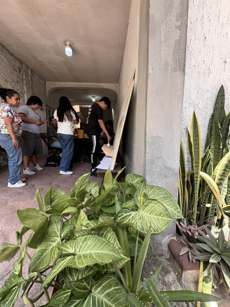 El pasillo del taller visto desde las plantas: el tablero recargado en la pared y varias personas pintando y conversando
