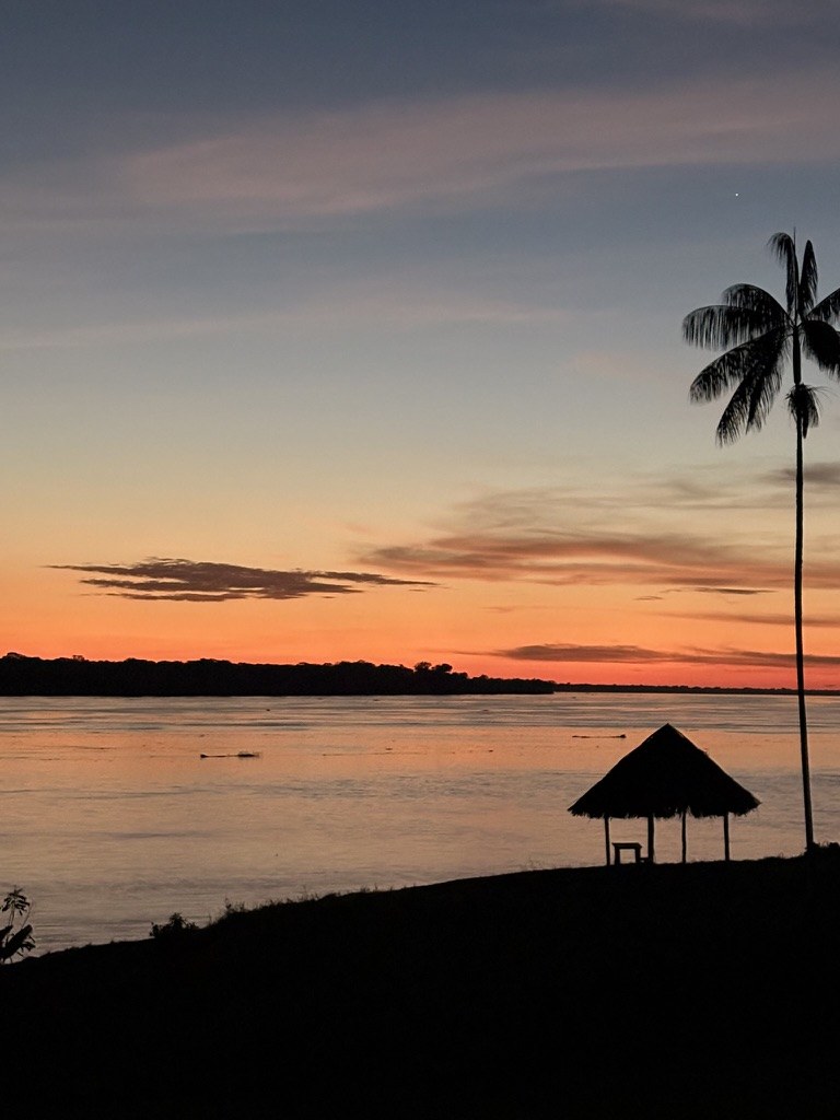 El río al atardecer, con un pequeño techo de palma en la orilla y el cielo naranja sobre la otra ribera