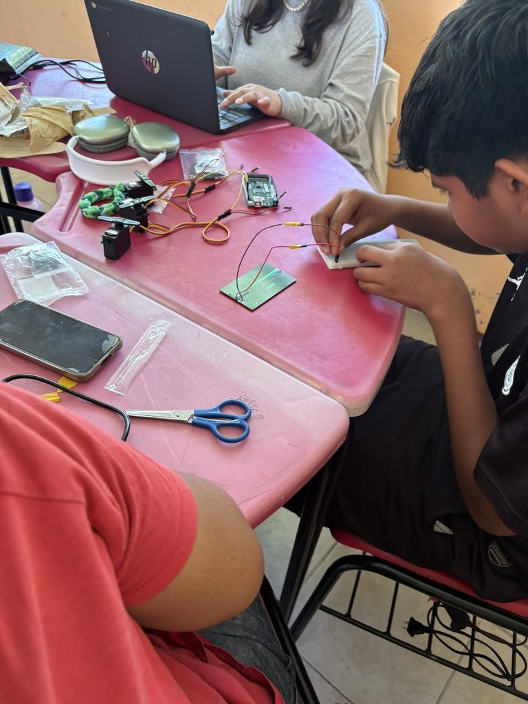 J&oacute;venes en una mesa preparando un circuito, con una laptop, placas y cables entre ellos