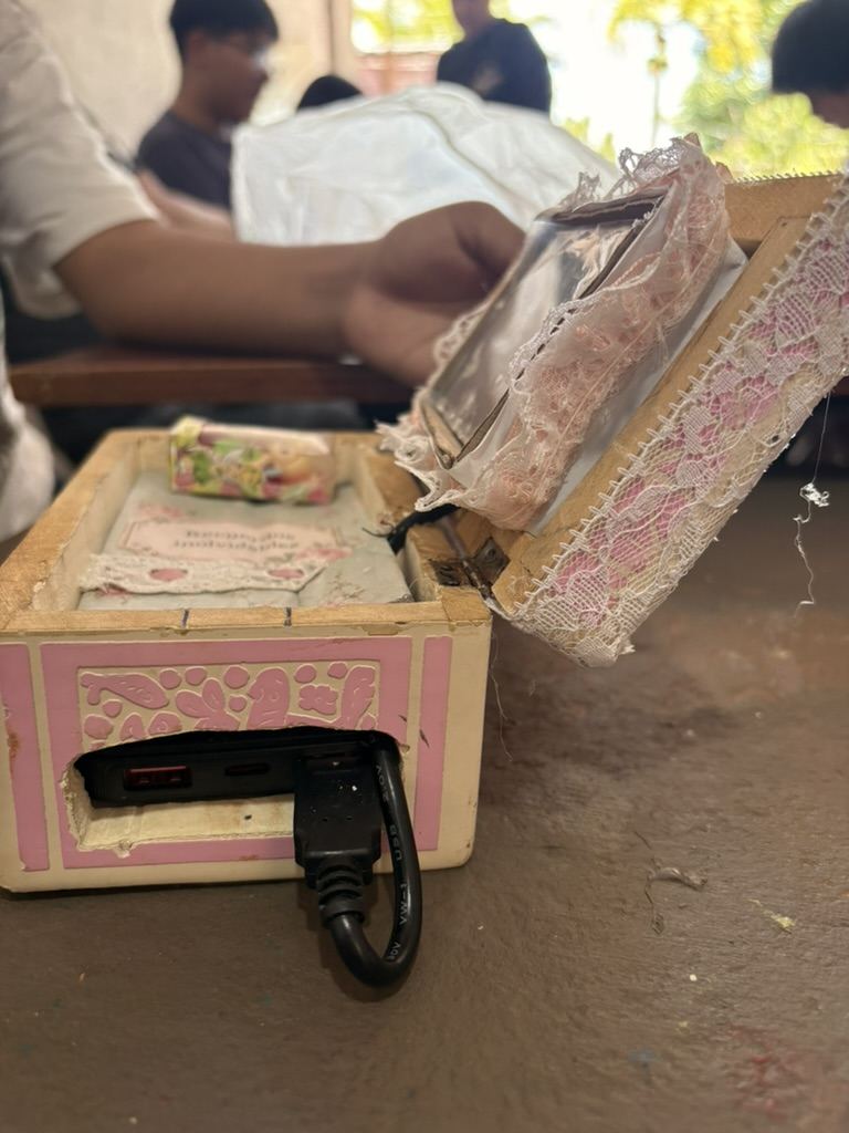 Una caja pintada de rosa y blanco, abierta, con la bater&iacute;a y un cable saliendo por un costado
