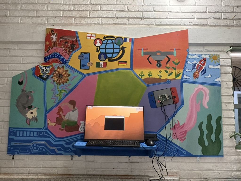 El mural montado en la pared con una computadora conectada abajo y una Raspberry Pi sujeta sobre una consola pintada