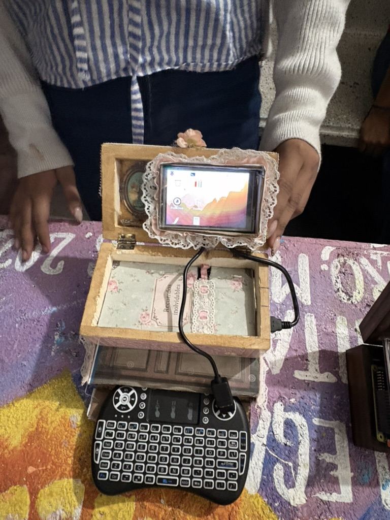 Unas manos sosteniendo abierta una caja forrada de encaje con la pantalla encendida, conectada a un teclado peque&ntilde;o