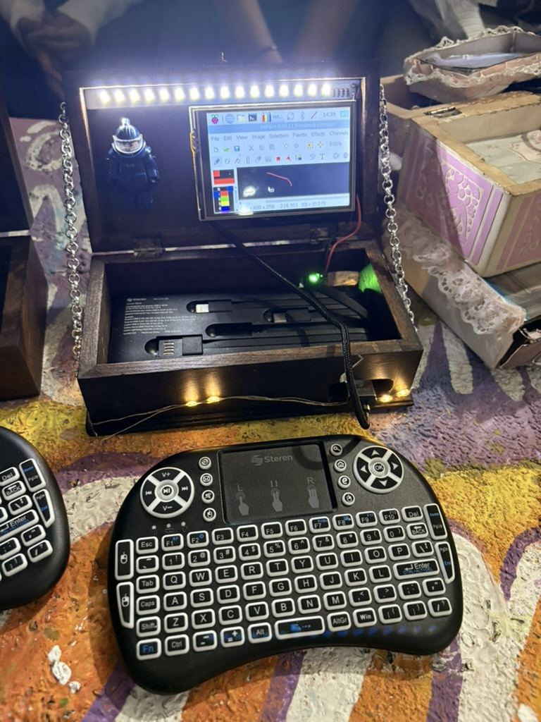 Una caja de madera oscura abierta como computadora: la pantalla encendida en la tapa, una tira de leds iluminando y un teclado peque&ntilde;o enfrente