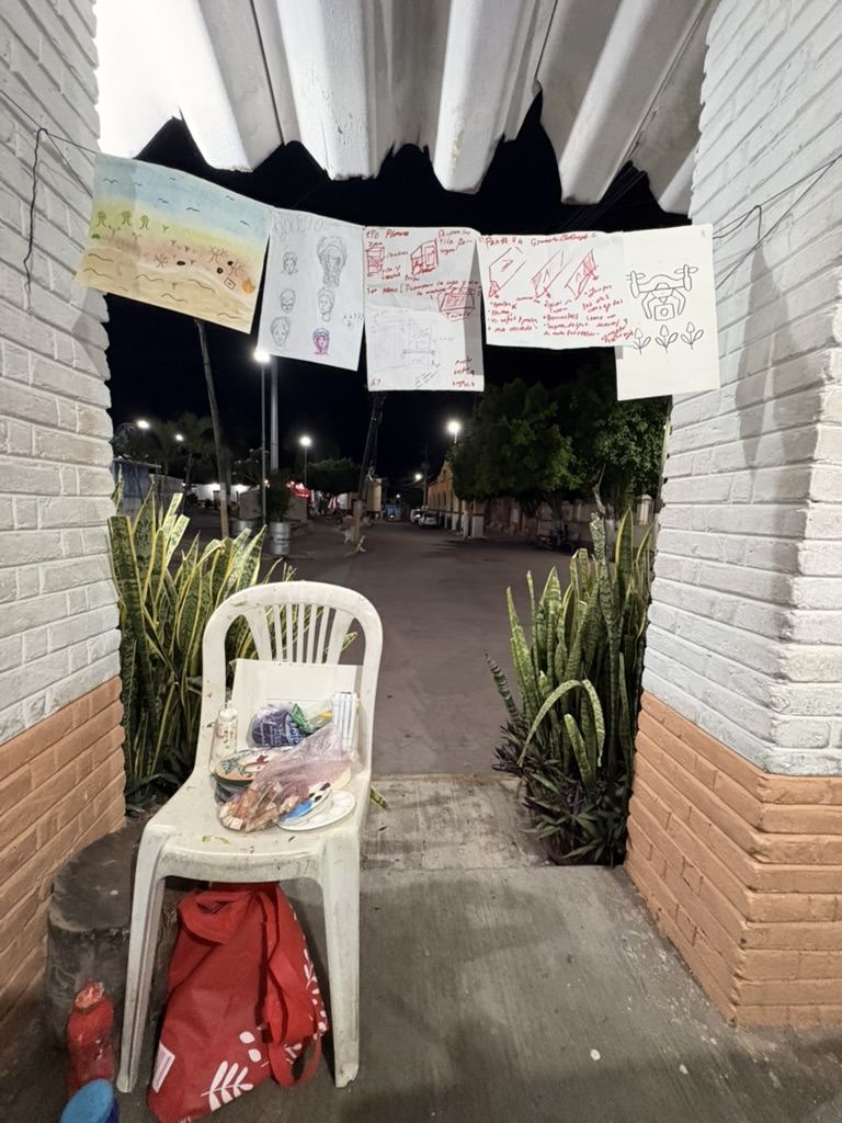 La entrada del lugar de noche, con dibujos y hojas de notas colgados de un cordel y una silla con paletas de pintura debajo