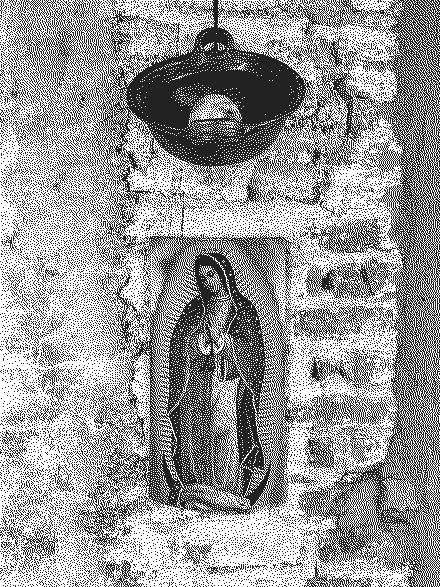 Un cuenco de barro colgado con un membrillo dentro y, más abajo, una imagen impresa de la Virgen de Guadalupe sobre una pared de ladrillo encalado