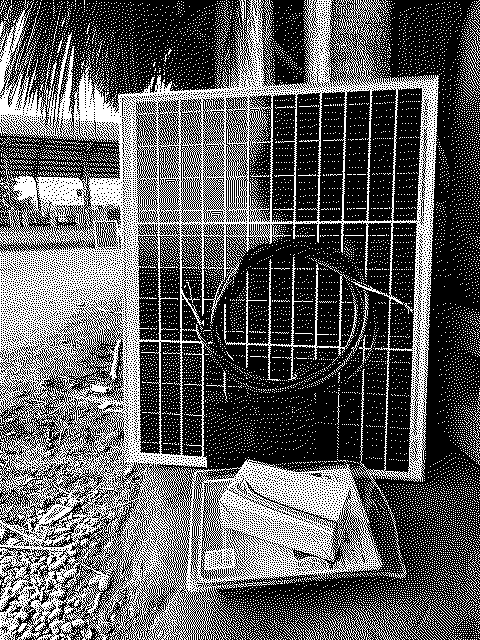 Un panel solar apoyado sobre una caja en el suelo en Maguaré, con el río y un techo de palma detrás