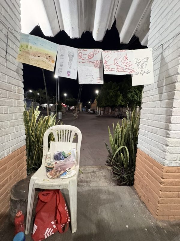 La entrada en arco de un espacio en Quebrantadero de noche, con dibujos colgados de un cordel y la calle al fondo