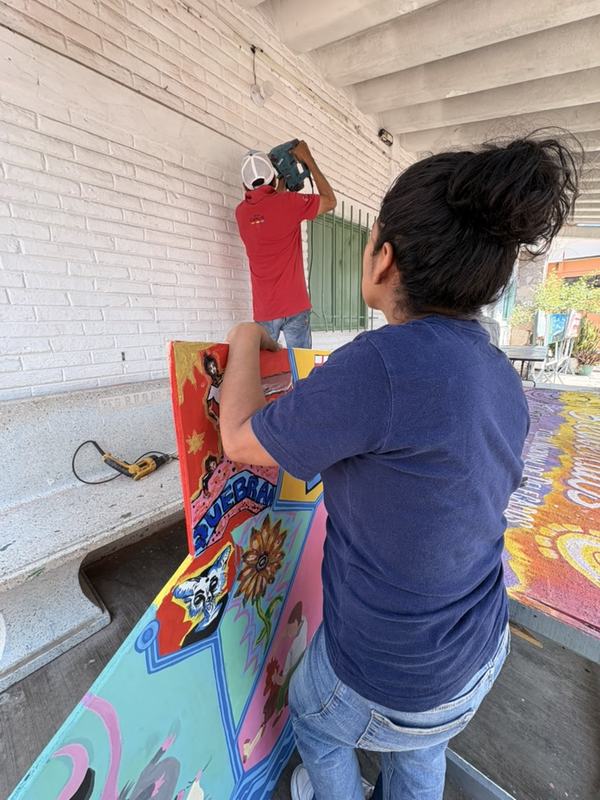 Un joven de espaldas, subido a una silla, fija una pieza del mural en lo alto de la pared