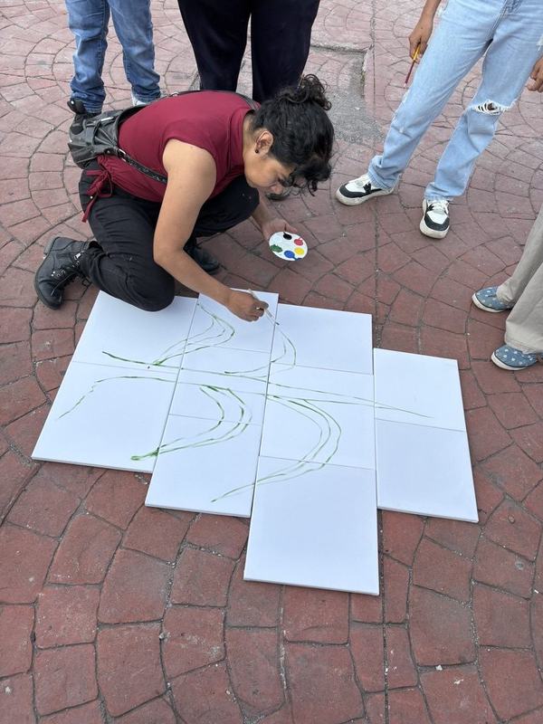 Una joven arrodillada dibuja sobre lienzos blancos puestos en el suelo de la plaza